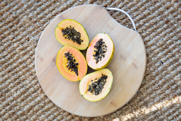 Two halves of a fresh papaya placed on a round wooden cutting board, resting on a textured woven...