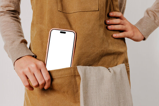 Woman showing smartphone with blank screen in apron pocket