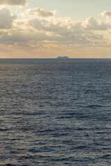 Obraz premium vertical sea view with beautiful water, horizon and warn golden sky, and the silhouette of a cruise ship in the distance