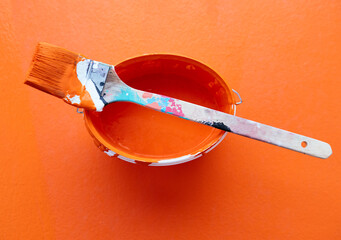 Bright orange paintbrush resting on a container filled with pink paint