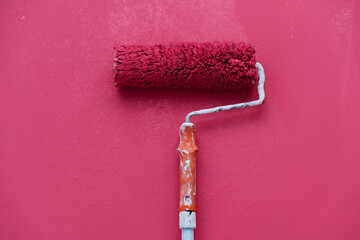 A paint roller rests on a pink wall