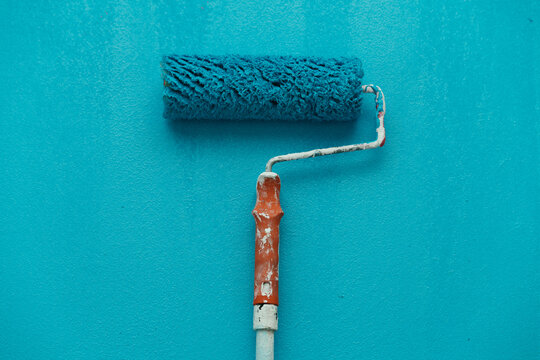 A paint roller rests on a blue wall