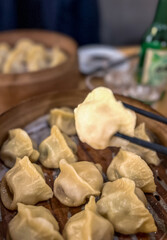 Asian dumplings in a wooden bowl on a wooden table with a bottle with soju on the background