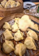 Asian dumplings in a wooden bowl on a wooden table with a bottle with soju on the background