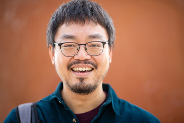 Portrait of an Asiatic smiling man with glasses standing against an orange background