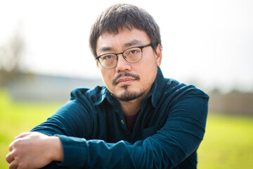 Thoughtful Asian man with glasses in outdoor park setting