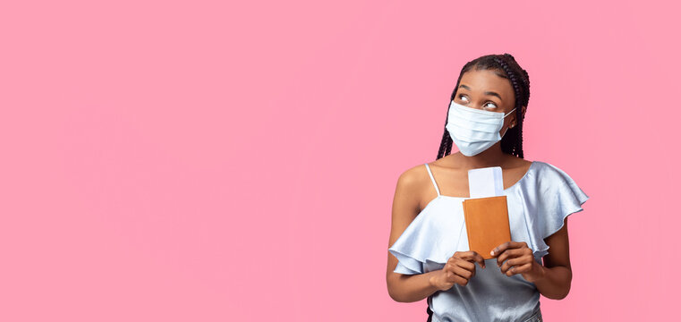 Traveling during coronavirus epidemic. Young black woman wearing face mask, holding passport and plane tickets, looking aside at empty space on pink studio background, banner design