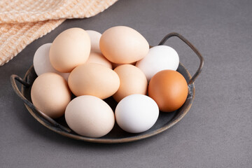 A collection of fresh eggs displayed in a rustic bowl on a textured countertop with a soft cloth in the background