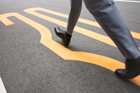 Businessperson walking along yellow road markings on asphalt
