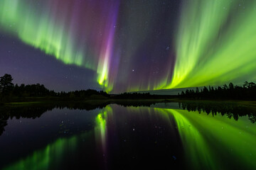 Northern lights in Kiruna, Sweden, reflecting on calm water in September with stars and forest in the background.