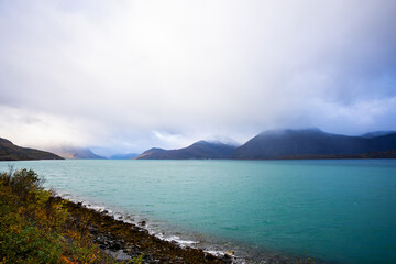 Autumn landscape of the Lyngen Alps in Northern Norway with snowy peaks, dramatic clouds, and a tranquil fjord.