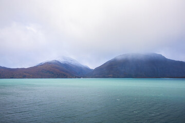 Autumn landscape of the Lyngen Alps in Northern Norway with snowy peaks, dramatic clouds, and a tranquil fjord.