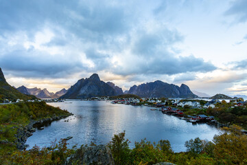 Autumn sunset in Reine, Lofoten Islands, Norway, with dramatic mountains, calm waters, and traditional houses along the shore.