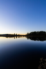 A peaceful sunset over a lake in Lapland, Sweden, with the reflection of trees in the still water.