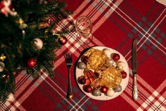 Christmas tree and plate with colorful festive balls are the table.
