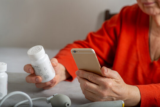 Mature woman scrolling phone while holding a pills bottle
