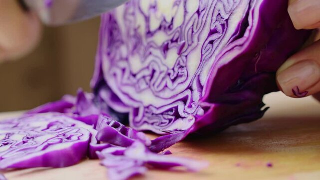 Female hands cutting and slicing purple cabbage with knife on wooden board
