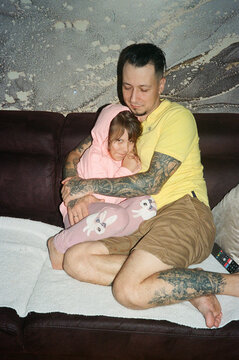 A father hugs his young daughter while sitting on the couch