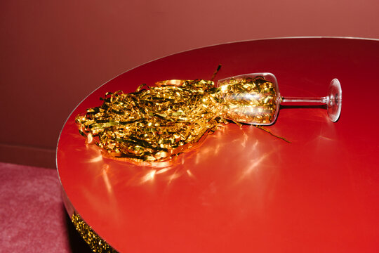 Spilled Wine Glass with Gold Confetti on Red Table