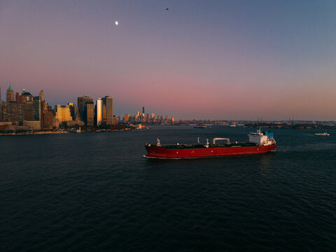 Wide view of cargo ship and city skyline at sunset.