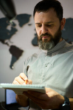 Man writing in notebook while standing before a world map in an office