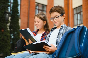 Children read books sitting on bench in school yard. Back to school. Beginning of school lessons