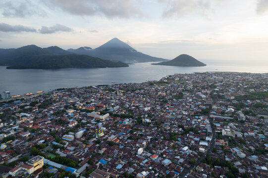 Aerial view of a coastal Indonesian city with volcanoes in background