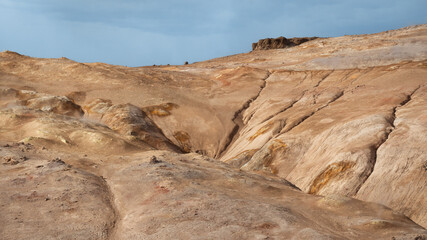 Geothermal terrain with steaming vents, golden-orange soil, and rocky formations near Námafjall, Iceland.