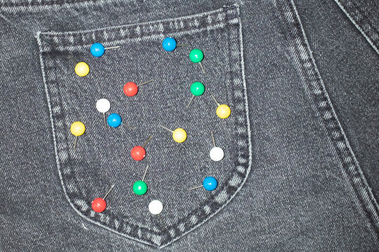 Close-up of jeans with colourful office supply paper pins on a pocket