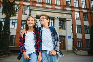 Happy school kids friends boy and girl with backpacks walking and laughing having fun together near school building outside outdoor after lessons