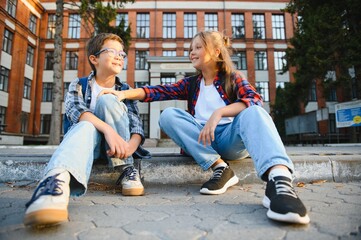 Fototapeta premium Happy schoolchildren near the school. A boy and a girl are primary school students. School friendship