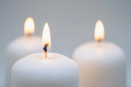 Three white candles lit in a row, often used as decoration or symbolization