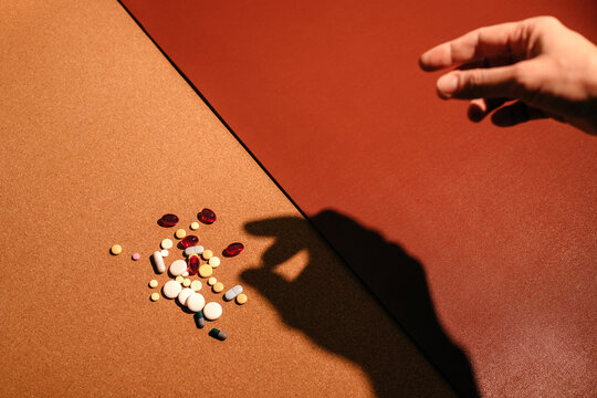 Woman's hand touching colorful pills over brown table.