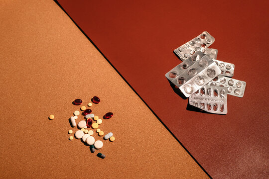 Stack pf colorful pills and empty blisters over brown backdrop.