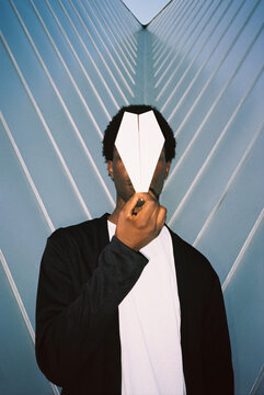 Man hiding face with paper airplane against modern geometric backdrop