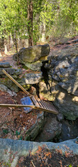 Wooden ladder into a dark rocky crevice with large granite rock, under coniferous trees. 