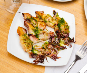 Roasted calamari with pesto sauce dished up in a plate on the laid restaurant table