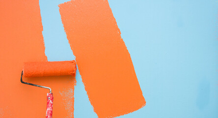 A paint roller is painting with blue and orange colors indoors