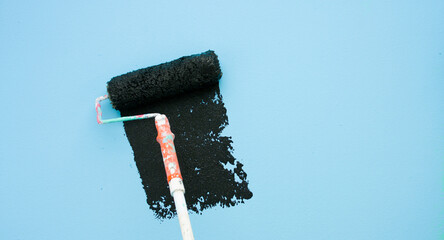 A paint roller is painting with blue and black colors indoors