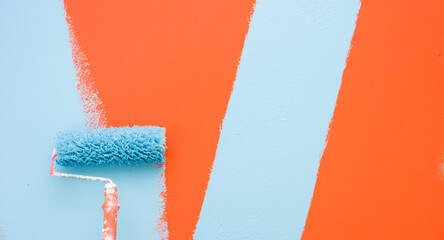 A paint roller is painting with blue and orange colors indoors