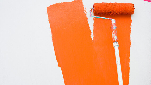 A paint roller is painting with pink and white colors indoors