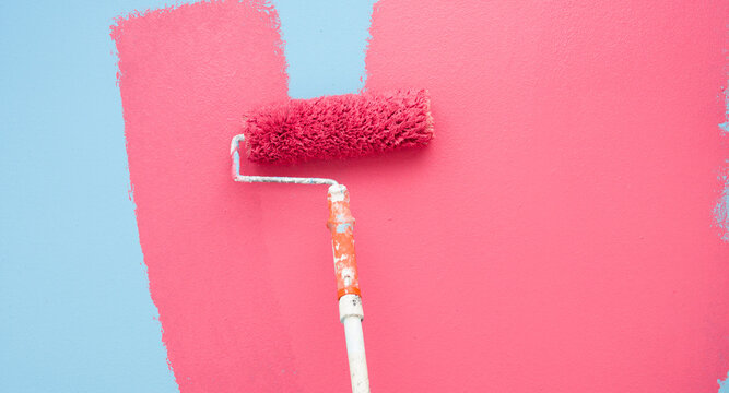 A paint roller is painting with pink and blue colors indoors
