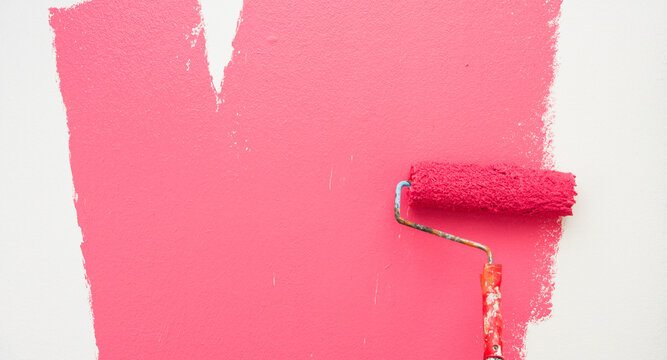 A paint roller is painting with pink and white colors indoors