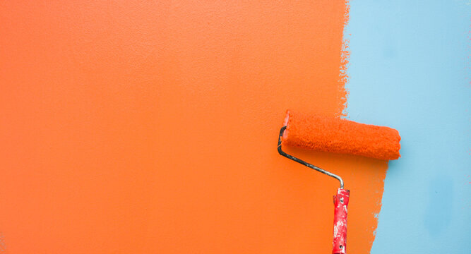 A paint roller is painting with blue and orange colors indoors