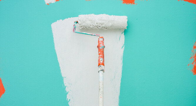 A paint roller is painting with white and turquoise indoors