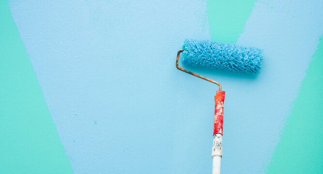 A paint roller is painting with blue and green colors indoors