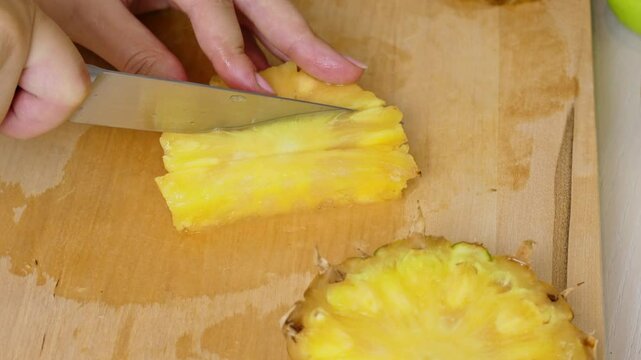 Female hands cutting and slicing yellow pineapple with knife on wooden board