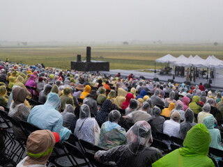 Crowd wearing colourful plastic ponchos sit waiting in the rain.