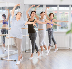 Group of women beginners rehearsing ballet moves at barre in dance studio