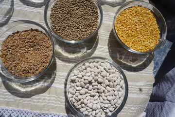 Τhree glass bowls placed on a table outdoors with fine cretan products, dry beans, lentils and wheat seeds